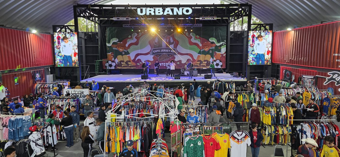 Vista panorámica del evento: pasillos con racks de jerseys, asistentes recorriendo y escenario al fondo